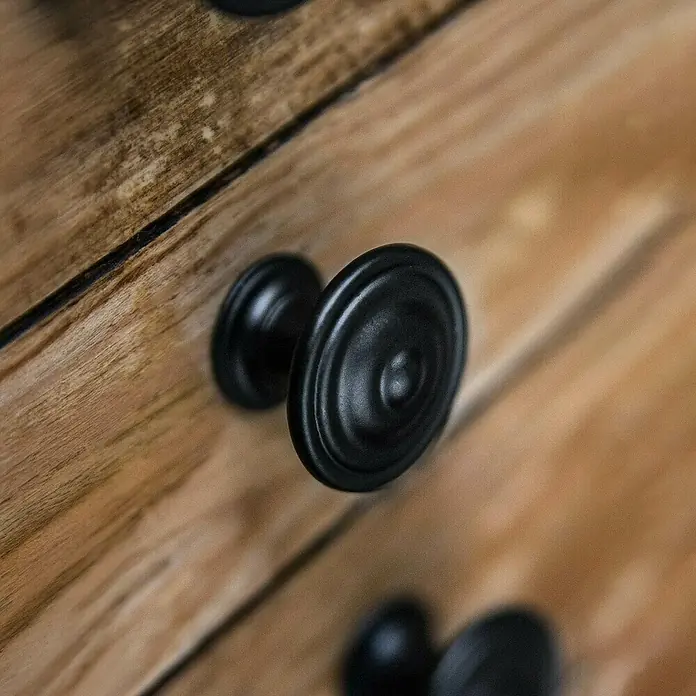 Rei Möbelknopf - Ø x H: 35 x 26 mm, Schwarz - Zwei schwarze, texturierte Schubladenknöpfe an einer rustikalen Holzschrankoberfläche.