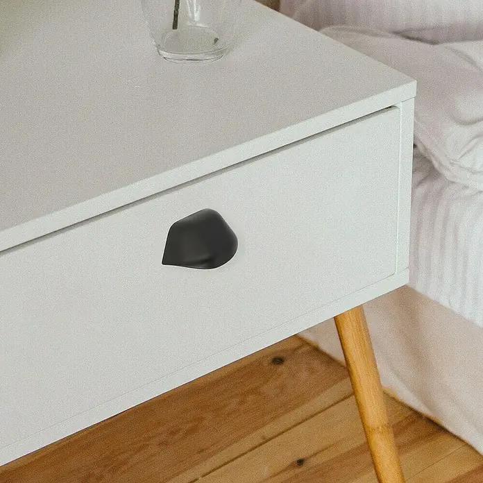 Rei Möbelgriff - Lochabstand: 64 mm, Sonstige, Schwarz - Ein matt schwarzer, organisch geformter Griff mittig auf einer weißen Schublade eines modernen Nachttischs.