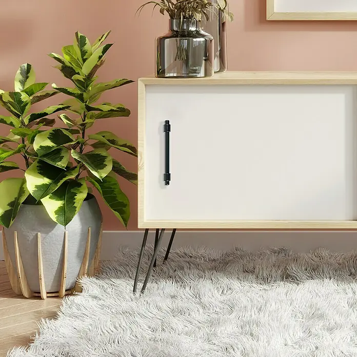 Rei Möbelgriff - Lochabstand: 96 mm, Sonstige, Schwarz, L x B x H: 127 x 14 x 39 mm - Holzkabinett mit weißer Tür und schwarzem Griff, auf Haarnadelbeinen, dekoriert mit Pflanze und weißem flauschigem Teppich.