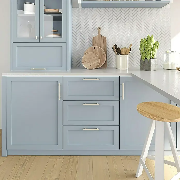 Rei Möbelgriff - Lochabstand: 128 mm, Stahl, Grau - Moderne Küche mit hellblauen Schränken, weißer Arbeitsplatte und weißem Fischgrät-Spritzschutz. Ein Holz-Barhocker steht an der Theke.