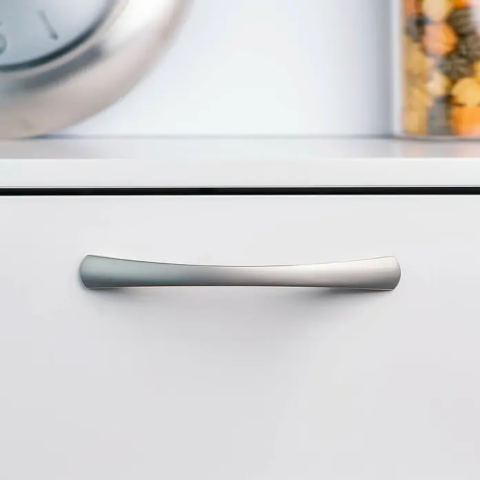 Rei Möbelgriff - Lochabstand: 128 mm, Aluminium, Matt Chrom - Satinierter, silberfarbener, gebogener Metallgriff an einer weißen Schublade oder einem Schrank.
