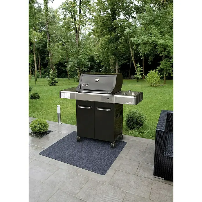 Alfombra exterior ignífuga barbacoa - Gris - Imagen de una parrilla Weber Spirit en un patio con una estera gris, rodeada de vegetación.