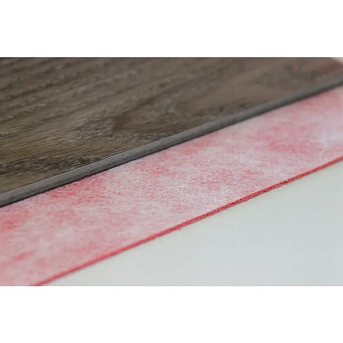 b!design Unterlagsmatte - 10 m², Stärke: 1,4 mm - Nahaufnahme einer braunen Holzoptik-Bodenplatte mit grauer Kante und roter Faserunterlage.