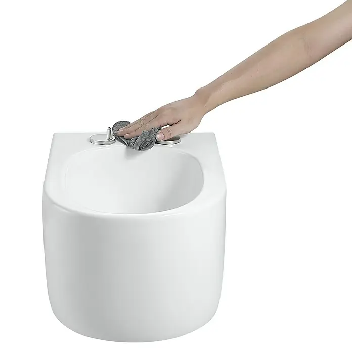 Camargue Wand-WC-Set Amsterdam - Spülrandlos, Ohne Spezialglasur, Spülform: Tief, WC Abgang: Waagerecht, Weiß - Eine Hand reinigt ein elegantes weißes Bidet mit einem grauen Mikrofasertuch.
