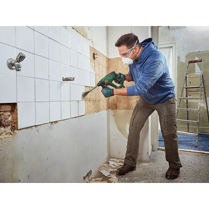 Bosch Professional AMPShare 18V Akku-Kombihammer UniversalHammer 18V - 18 V, 1 Akku, 4 Ah, 2 J - Mann in Schutzausrüstung verwendet ein grünes und schwarzes Elektrowerkzeug, um weiße Fliesen von einer Wand zu meißeln.