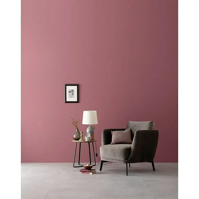 SCHÖNER WOHNEN-Farbe Wandfarbe Designfarbe - Englisches Rosenrot, Matt, 2,5 l, Konservierungsmittelfrei - Stilvolles Interieur mit einem grauen Sessel und einem Beistelltisch mit Lampe, Vase und Dekoration vor einer rosa Wand, das eine gemütliche Atmosphäre schafft.