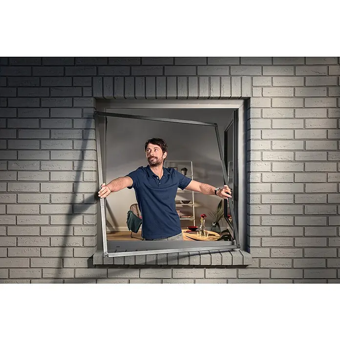 Tesa Insektenschutzfenster FALT für Fenster - Weiß, Montage Insektengitter: Klemmen - Mann hält ein dunkelgraues Fliegengitter in einer Fensteröffnung.