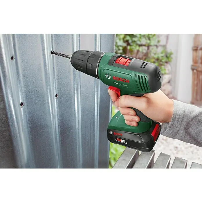 Bosch Power for All 18V Akku-Bohrschrauber Easy Drill 18V-40 - 18 V, 2 Akkus, 1,5 Ah, 32 Nm - Grüner und schwarzer Bosch EasyDrill 18V-40 Akkuschrauber, von einer Hand gehalten, bohrt ein Loch in Wellblech.