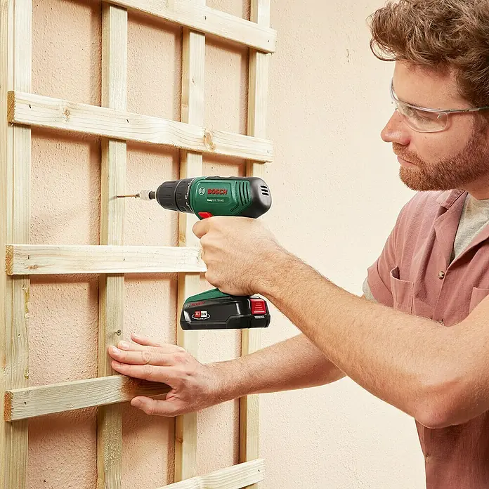 Bosch Power for All 18V Akku-Bohrschrauber EasyDrill 18V-40 - 18 V, 1 Akku, 1,5 Ah, 32 Nm - Mann befestigt mit grün-schwarzem Bosch EasyDrill 18V-40 Akkuschrauber ein Holzspalier.