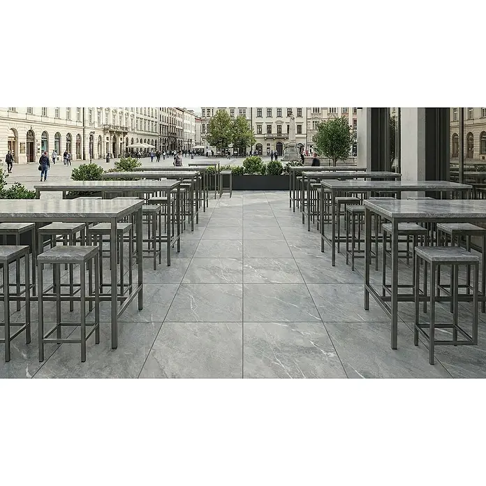 Terrassenfliese Total Stone - 60 x 90 x 2 cm, Grigio, Matt - Robuste graue Fliesen mit dezentem Marmoreffekt bilden den weitläufigen Boden einer Außenterrasse mit Stehtischen und Hockern.