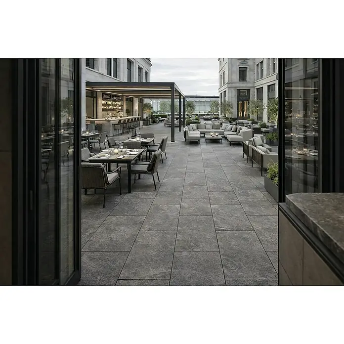 Terrassenfliese Total Stone - 60 x 90 x 2 cm, Grafit, Matt - Dunkelgraue Outdoor-Terrassenfliesen in Steinoptik im versetzten Muster, die den Boden einer großen Restaurantterrasse bilden.