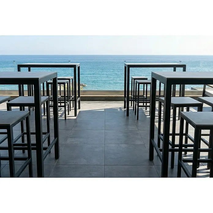 Terrassenfliese Urban Pro - 60 x 60 x 2 cm, Anthrazit, Matt - Schwarze Metall-Stehtische und Hocker auf einer Terrasse mit Meerblick.