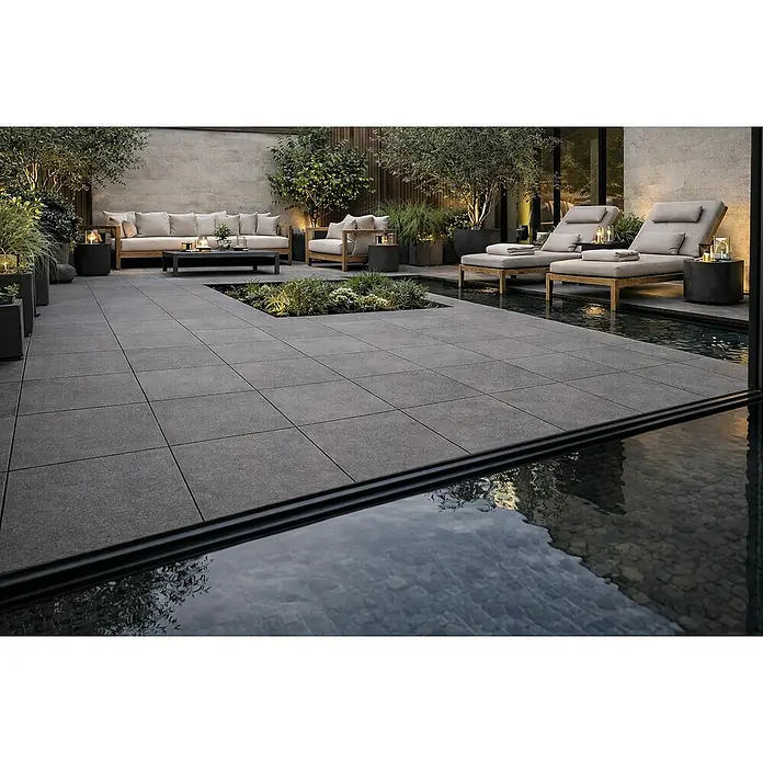 Terrassenfliese Colosseo - 60 x 60 x 2 cm, Basalt Grau, Matt - Dunkelgraue quadratische Outdoor-Pflastersteine bilden einen modernen Terrassenboden, umgeben von Lounge-Möbeln und Wasser.