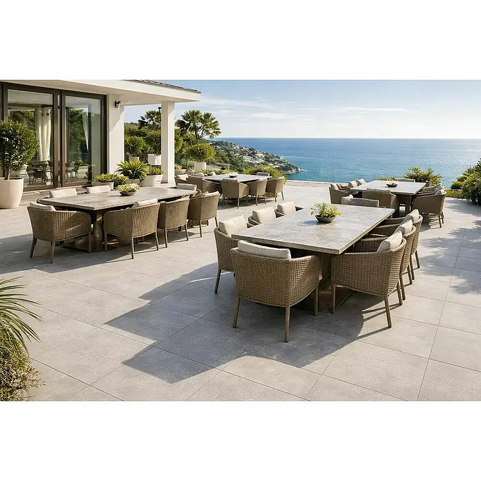 Terrassenfliese Urban Pro - 60 x 60 x 2 cm, Grey, Matt - Mehrere Outdoor-Essgruppen mit geflochtenen Stühlen, hellen Kissen und Steintischen auf einer Terrasse mit Meerblick. Ideal für Speisen im Freien.