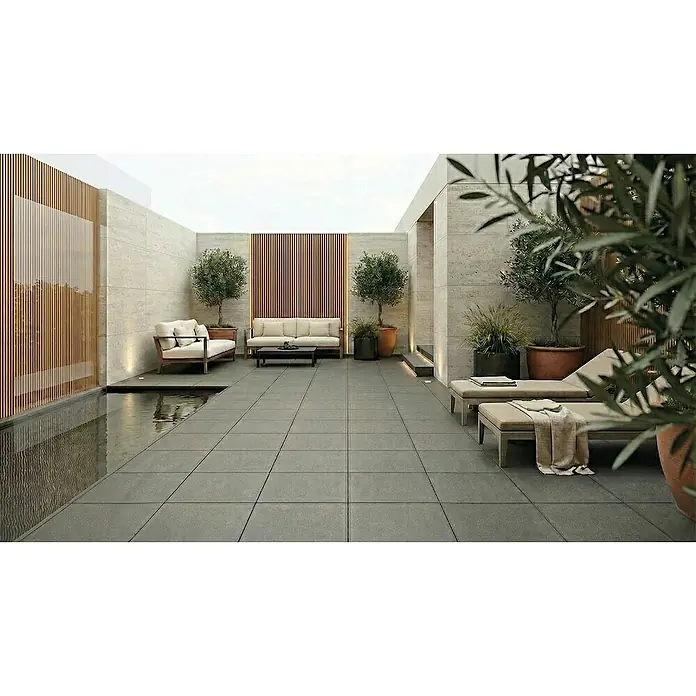 Granulati Zandobbio Terrassenfliese Colosseo - 60 x 60 x 2 cm, Basalt Grau, Matt - Moderne Außenterrasse mit hellgrauen Bodenfliesen, hellen Sofas, Liegen, Olivenbäumen in Töpfen und einem schmalen Wasserbecken, das einen ruhigen Entspannungsbereich schafft.