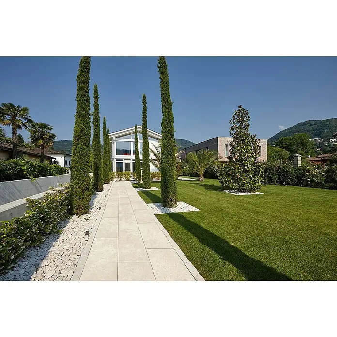 Terrassenfliese Torre - 40 x 80 x 2 cm, Botticino, Matt - Ein heller, gefliester Gartenweg führt durch einen gepflegten Garten mit hohen Zypressen und weißem Kies.