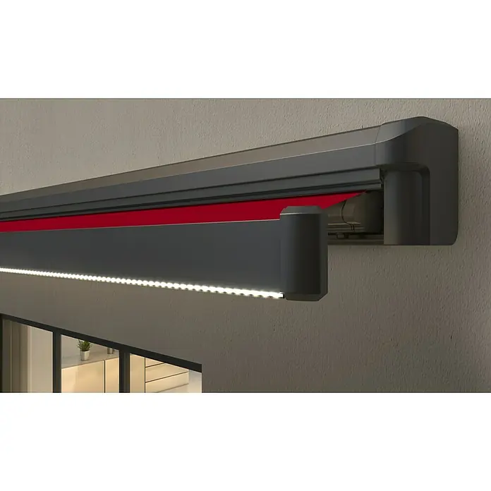 Spettmann LED-Vollkassettenmarkise Sunlite - Bordeaux, Farbe Gestell: Eisenglimmer matt, Breite: 3,5 m, Ausfall: 2,5 m - Dunkelgraue Markise mit rotem Stoff und integrierter LED-Beleuchtung, an einer Hauswand über einem Fenster montiert.