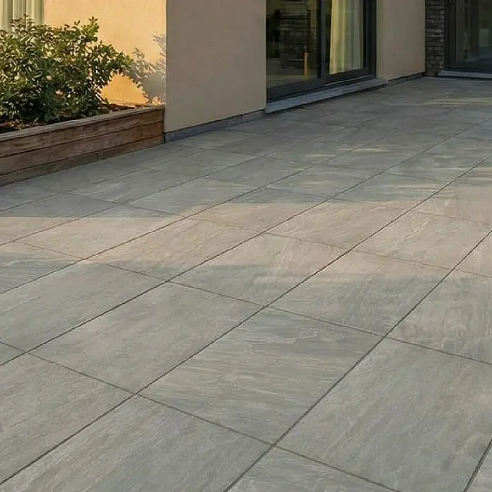 Terrassenfliese Tempio - 60 x 90 x 2 cm, Grey, Matt - Helle, strukturierte, rechteckige Terrassenplatten pflastern eine Außenterrasse neben einem Haus.