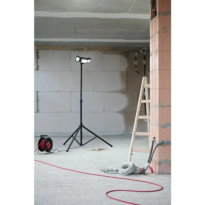 Profi Depot LED-Strahler - 42 W, 4.000 lm, 6.500 K, IP54 - Blick auf eine Baustelle mit einer tragbaren LED-Arbeitsleuchte auf einem Stativ, die den Raum ausleuchtet, umgeben von Baumaterialien.