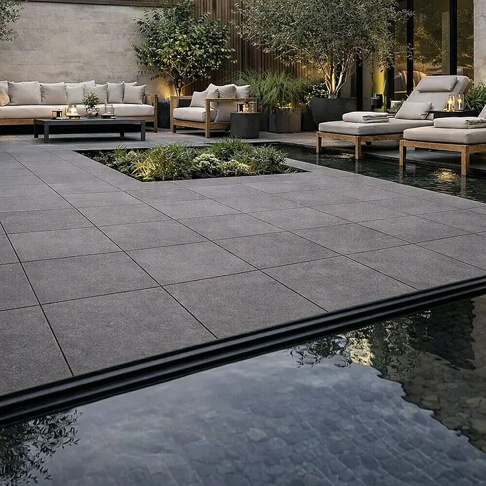 Terrassenfliese Colosseo - 60 x 60 x 2 cm, Basalt Grau, Matt - Große graue Outdoor-Pflasterplatten bilden eine moderne Terrasse mit Sitzgelegenheiten und Wasserspiel.