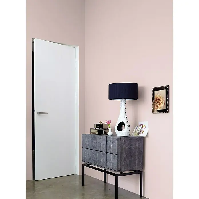 Alpina Wandfarbe Feine Farben - Wolken in Rosé, Matt, 2,5 l, Konservierungsmittelfrei - Elegantes Interieur mit einer grauen Kommode auf einem Metallgestell, die eine stilvolle Lampe und dekorative Objekte trägt, vor einer zartrosa Wand.