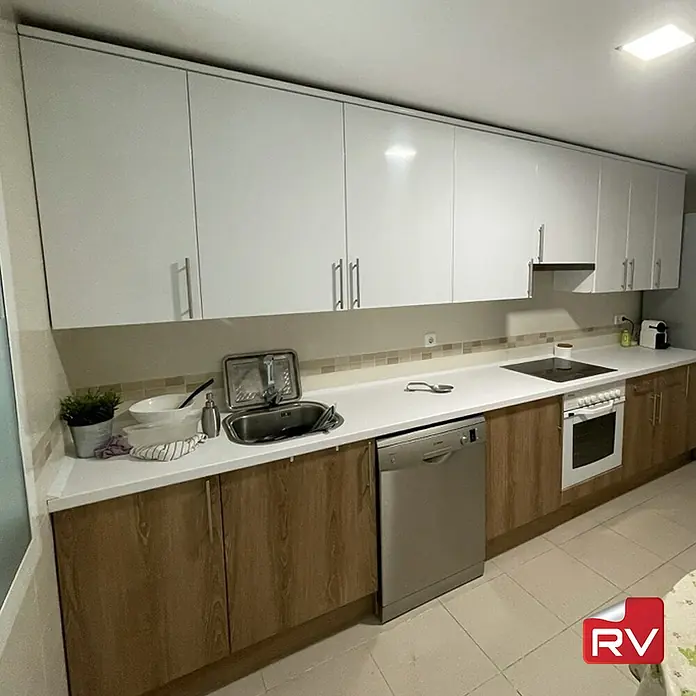 Lámina decorativa autoadhesiva vinílico autoadhesivo a metros - Blanco alto brillo - Cocina moderna con armarios superiores blancos brillantes, muebles bajos efecto madera y electrodomésticos de acero inoxidable.