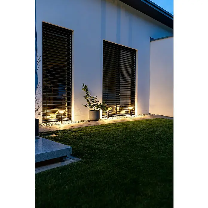 Osram Außenstehleuchte Endura Style solar -  - Moderne schwarze Pollerleuchten und lineare Wandleuchten beleuchten eine Hausfassade, einen Kiesweg und eine Topfpflanze bei Dämmerung mit warmweißem Licht.