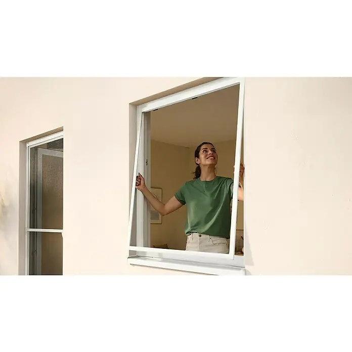 Tesa Insect Stop Insektenschutzgitter Premium - B x H: 100 x 100 cm, Anthrazit, Montage Insektengitter: Ankletten - Weißes Insektenschutzgitter wird von einer Frau in ein Fenster eingesetzt.