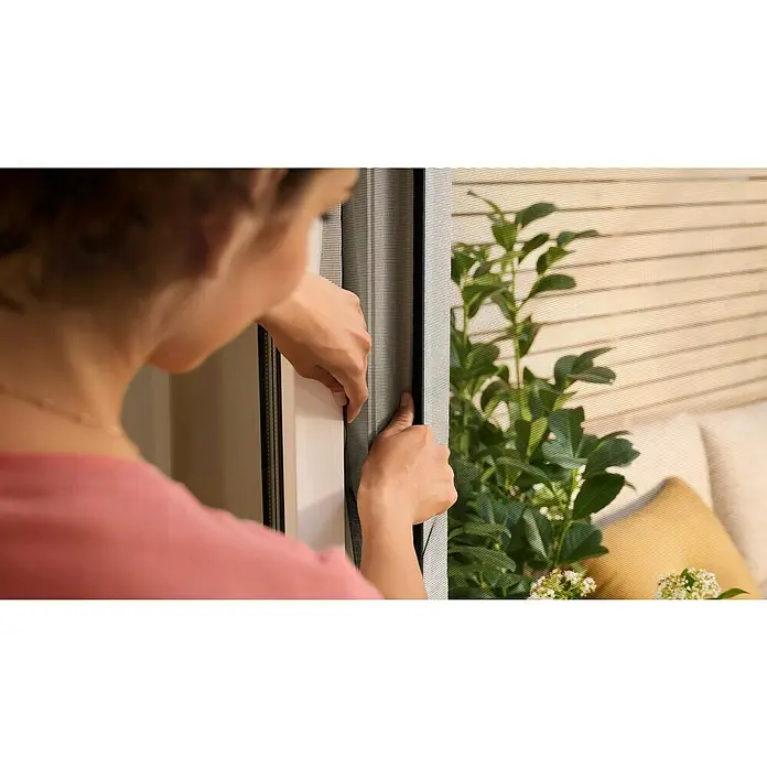Tesa Insect Stop Insektenschutzgitter Premium - B x H: 130 x 150 cm, Anthrazit, Montage Insektengitter: Ankletten - Hände stellen ein dunkles, plissiertes Insektenschutzgitter am Fenster ein.