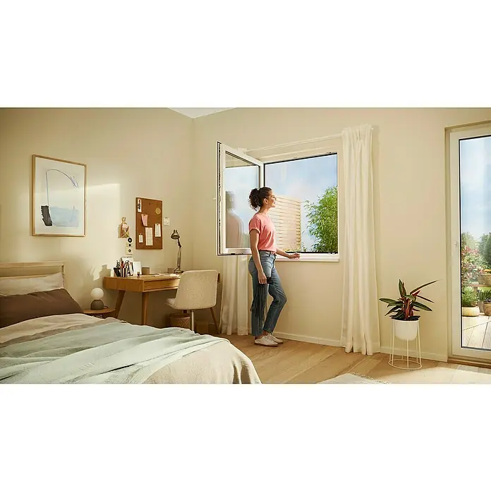 Tesa Insect Stop Insektenschutzgitter Premium - B x H: 130 x 150 cm, Anthrazit, Montage Insektengitter: Ankletten - Eine Frau steht an einem offenen Fenster mit einem dunklen Insektenschutzgitter, das frische Luft hereinlässt.