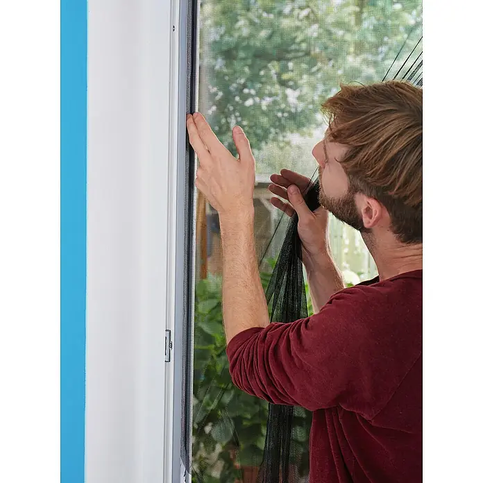 Tesa Insect Stop Insektenschutzgitter Premium - B x H: 120 x 250 cm, Weiß, Montage Insektengitter: Ankletten - Ein Mann installiert ein schwarzes Moskitonetz am Fensterrahmen, was seine Funktion als Insektenschutz zeigt.