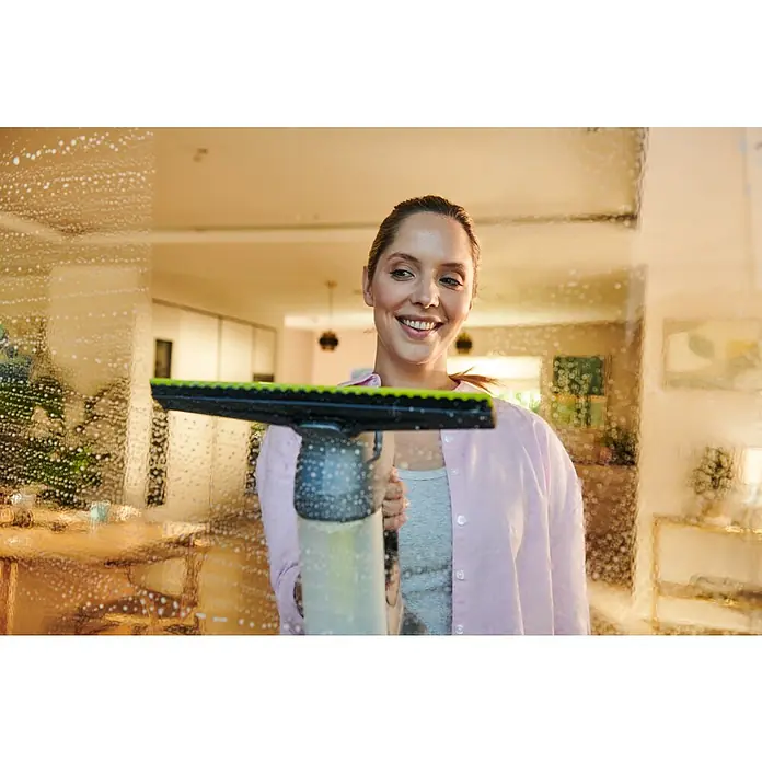 Ryobi ONE+ Akku-Fenstersauger RWV18-0 - 18 V, Ohne Akku - Lächelnde Frau reinigt schaumiges Fenster mit schwarzem und grünem Hand-Fensterreiniger.