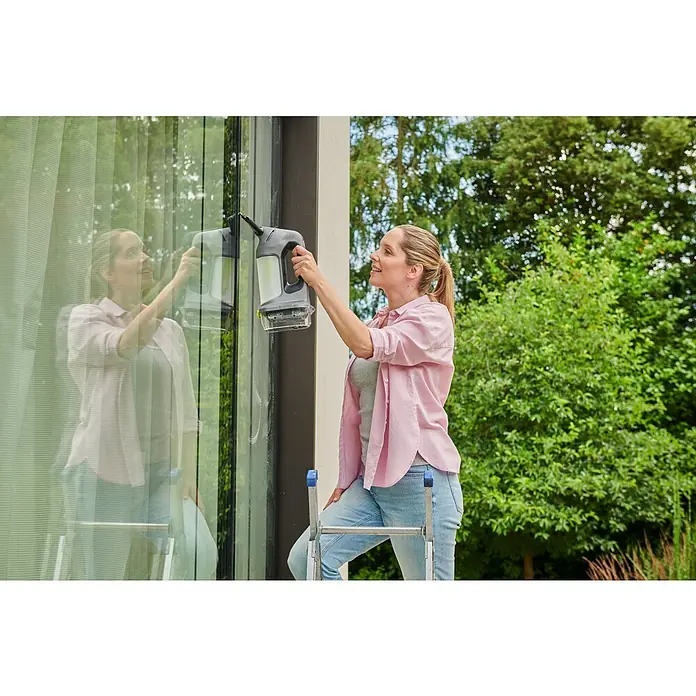 Ryobi ONE+ Akku-Fenstersauger RWV18-0 - 18 V, Ohne Akku - Frau reinigt ein großes Fenster mit einem grau-schwarzen Akku-Fensterreiniger.