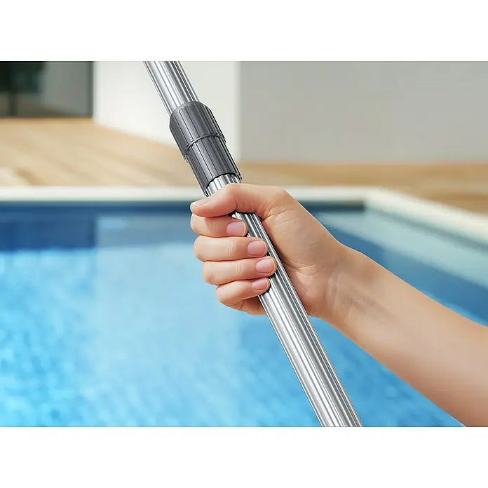 Mova Poolsauger Handler V10 - Akkubetrieben - Eine Hand hält eine silberne Teleskopstange mit grauem Verbinder vor einem verschwommenen Poolhintergrund.