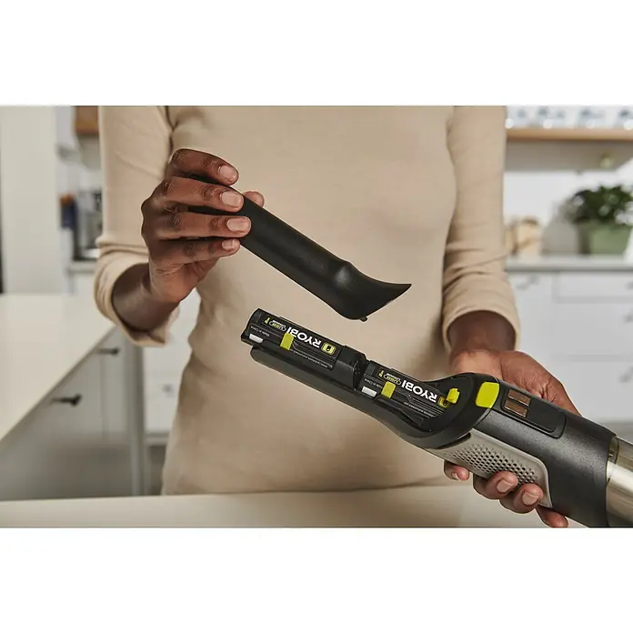 Ryobi Akku-Handstaubsauger RHV44-220G - 8 V, 2 Akkus, 2 Ah, Behältervolumen: 0,15 l - Eine Person steckt eine schwarze Fugendüse in einen schwarzen und grauen Handstaubsauger mit sichtbaren Ryobi-Akkus.