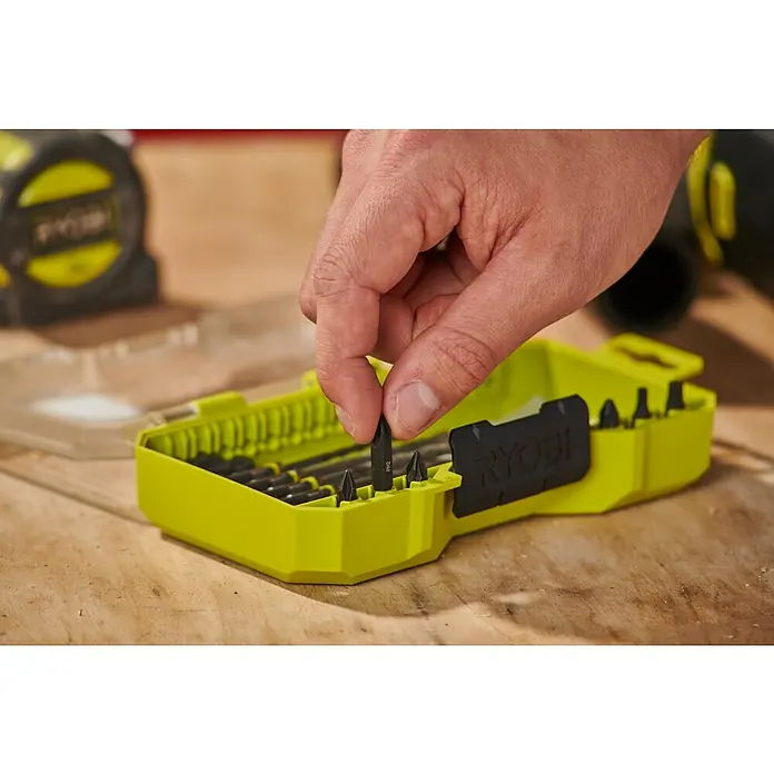 Ryobi Bohrer- & Bit-Set RARXMM7 - 13 -tlg. - Eine Hand entnimmt einen Schrauberbit aus einem limettengrünen Ryobi Bit-Set auf einer Werkbank.