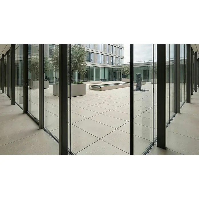 Terrassenfliese Duomo - 60 x 90 x 2 cm, Perla, Matt - Helle, großformatige quadratische Fliesen als eleganter Boden eines Außenhofs, umgeben von Glasgebäuden, Bäumen und einem Brunnen.