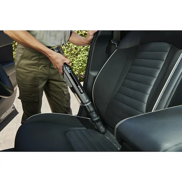 Ryobi Akku-Handstaubsauger RHV44-220G - 8 V, 2 Akkus, 2 Ah, Behältervolumen: 0,15 l - Schwarzer Ryobi Handstaubsauger reinigt einen Autositz.