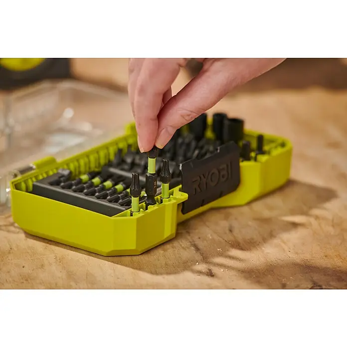 Ryobi Bit-Set RARXSD59 - 59 -tlg. - Eine Hand wählt einen schwarzen und neongrünen Ryobi Schrauberbit aus einem leuchtend grünen Bit-Set auf Holzunterlage.
