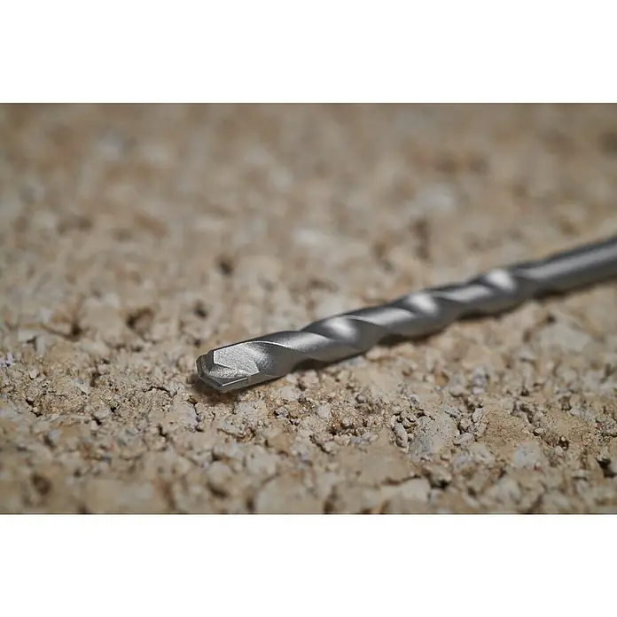 Ryobi Bohrer- & Bit-Set RARXM7 - 13 -tlg. - Metallischer Mauerwerksbohrer auf einer strukturierten Betonoberfläche.