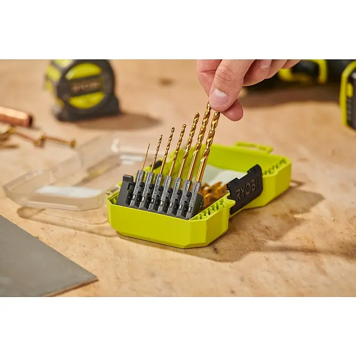 Ryobi Bohrer-Set RARXHG13 - 13 -tlg. - Eine Hand entnimmt einen goldfarbenen Bohrer aus einem Set verschiedener Größen in einer limettengrünen Ryobi-Hülle auf einer Holzwerkbank.