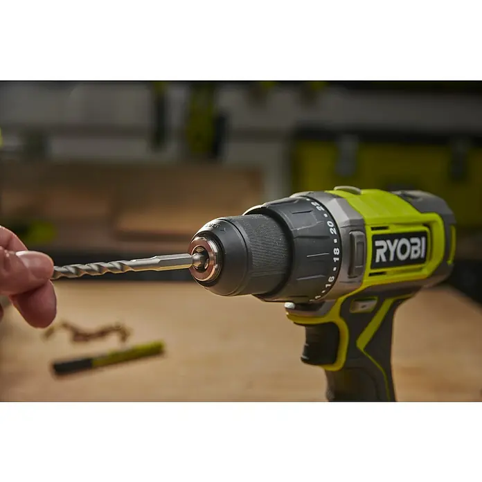 Ryobi Bohrer- & Bit-Set RARXM7 - 13 -tlg. - Eine Hand steckt einen Metallbohrer in das Bohrfutter eines grün-schwarzen Ryobi Akkubohrers.