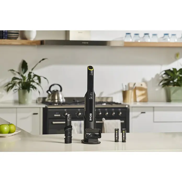 Ryobi Akku-Handstaubsauger RHV44-220G - 8 V, 2 Akkus, 2 Ah, Behältervolumen: 0,15 l - Schwarzer Ryobi Stabstaubsauger mit gelben Akzenten, Bürstenaufsatz und zwei Akkus auf einer Küchentheke.
