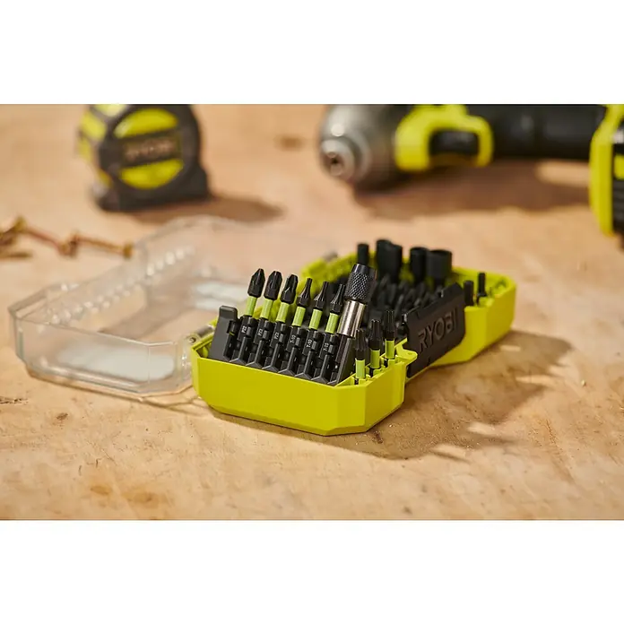 Ryobi Bit-Set RARXSD59 - 59 -tlg. - Hellgrünes und schwarzes Schrauberbit-Set mit verschiedenen Bits und einem Bithalter, auf einer Werkbank mit Werkzeugen.