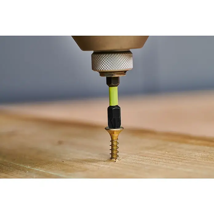 Ryobi Bit-Set RARXSD59 - 59 -tlg. - Ein Schraubendreherbit mit neongrünem Schaft treibt eine goldene Holzschraube in eine Holzoberfläche.