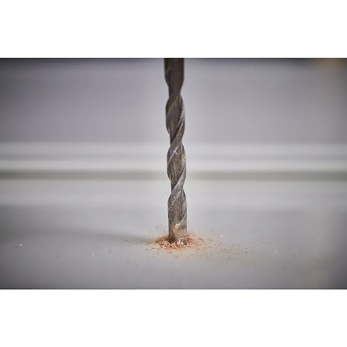 Ryobi Bohrer- & Bit-Set RARXMM7 - 13 -tlg. - Ein Metallbohrer bohrt in eine Oberfläche und wirbelt feinen braunen Sägemehl auf.