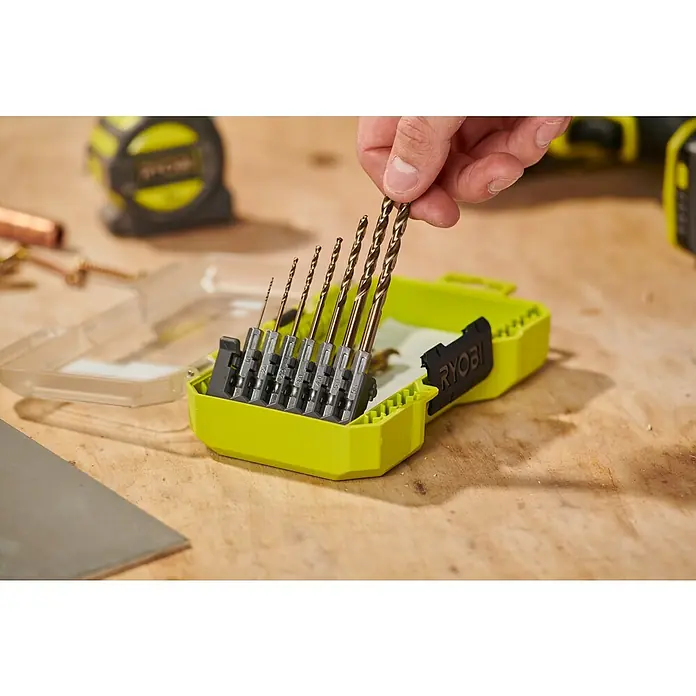 Ryobi Bohrer-Set RARXHGC10 - Metall, 10 -tlg. - Eine Hand wählt einen bronzefarbenen Bohrer aus einem neongrünen RYOBI-Bohrer-Set auf einer Holzwerkbank.