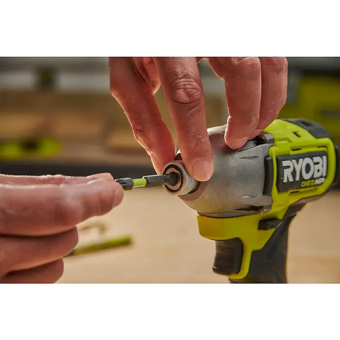 Ryobi Bit-Set RARXSD59 - 59 -tlg. - Eine Hand setzt einen schwarzen und neongrünen Bit in das silberne Bohrfutter eines grün-schwarzen Ryobi Schlagschraubers ein.
