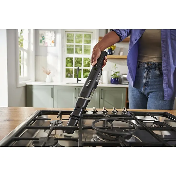 Ryobi Akku-Handstaubsauger RHV44-220G - 8 V, 2 Akkus, 2 Ah, Behältervolumen: 0,15 l - Schwarzer Ryobi Handstaubsauger reinigt Krümel von einem Gaskochfeld.