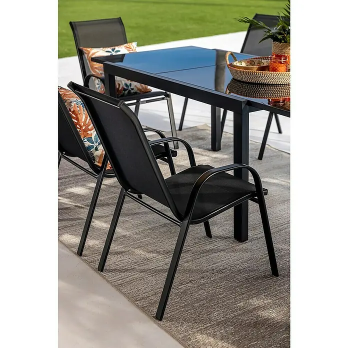 Silla de jardín Moliné - 76,5 x 53 x 93 cm, Antracita, Acero/Textiline, Apilable - Juego de comedor exterior de metal negro y malla con mesa de vidrio y sillas, con cojines estampados sobre una alfombra.